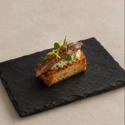 Brioche tostado, mantequilla de hierbas y anchoa.